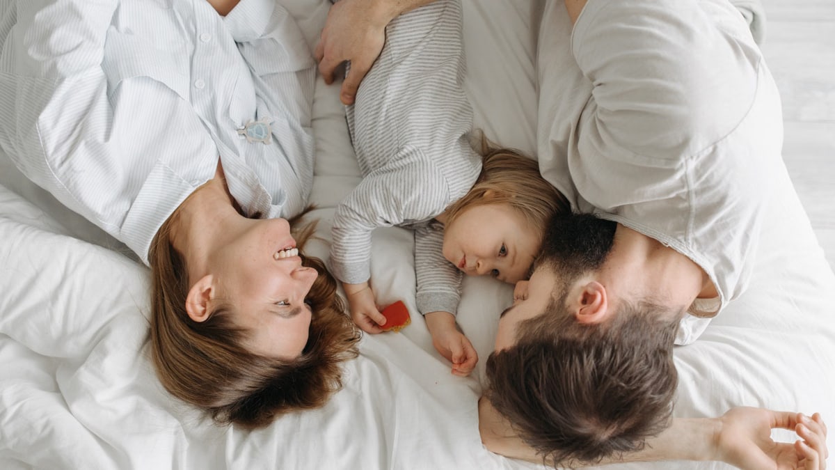 Father, mother, and daughter bonding on a bed, embracing family moments.